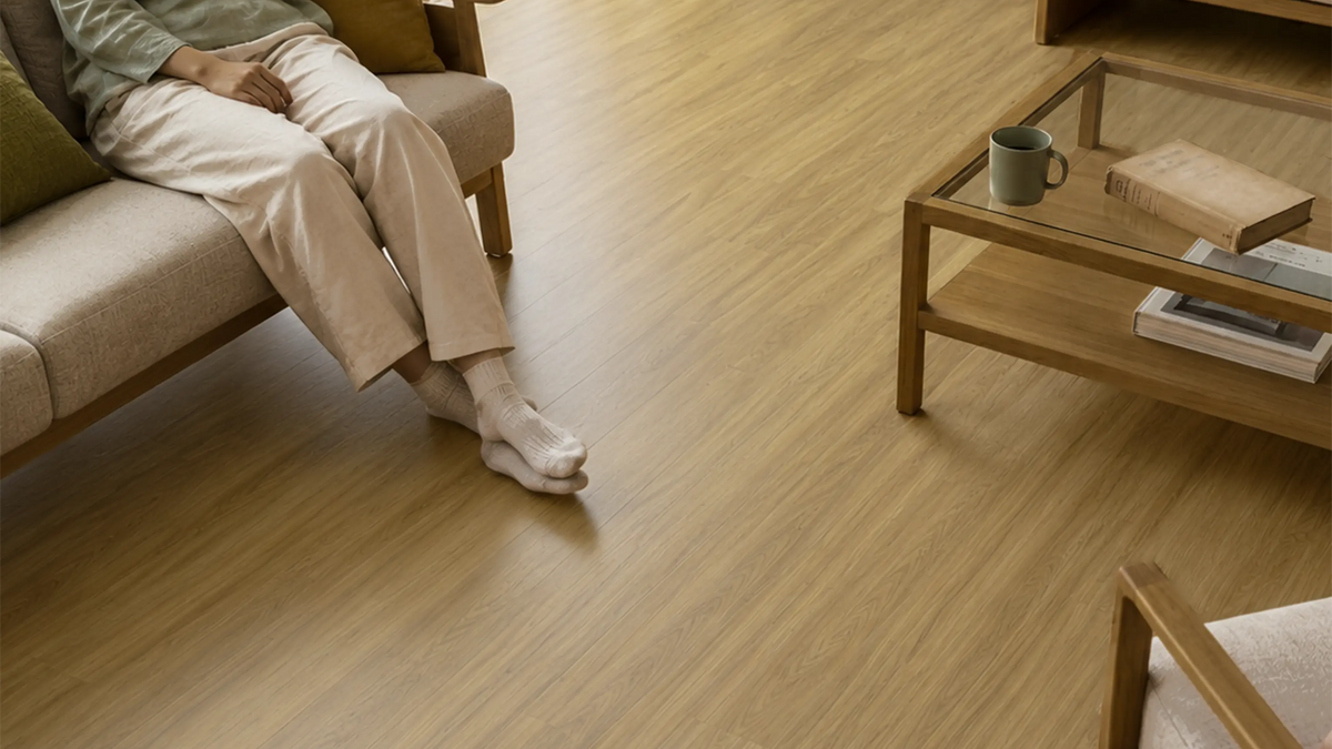 Coastal Blackbutt vinyl plank flooring in a living room, with a person in socks sitting on a sofa beside a coffee table