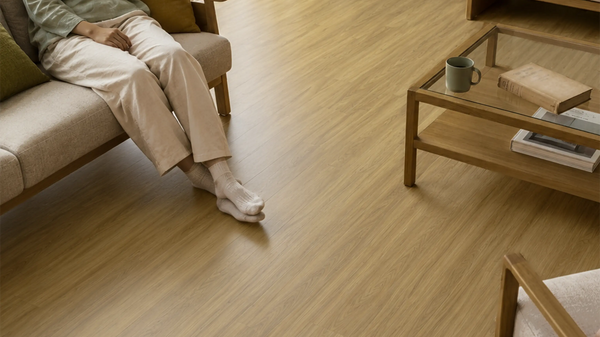 Coastal Blackbutt vinyl plank flooring in a living room, with a person in socks sitting on a sofa beside a coffee table