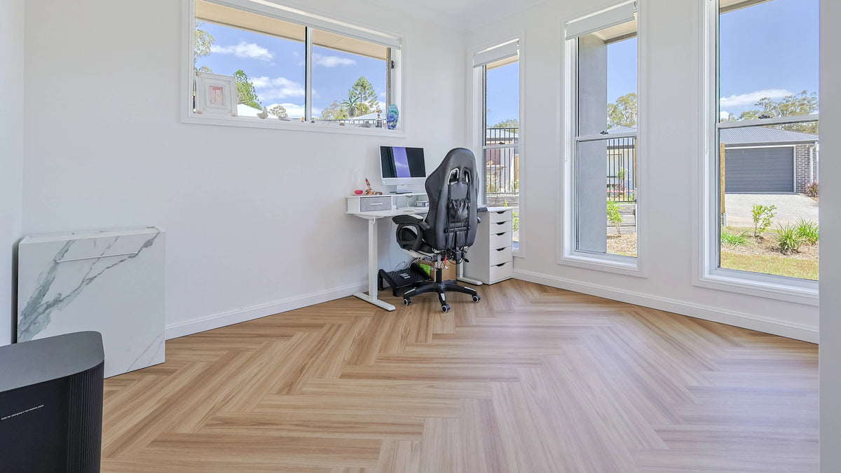Light oak herringbone vinyl plank flooring in a bright home office with a desk and tall windows