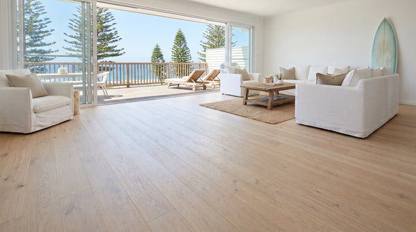 Coastal Australian living room with pale blonde hybrid flooring opening onto an ocean-view deck
