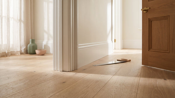 Pale oak hybrid floorboards fitted neatly under an undercut door jamb and architrave in a bright Australian hallway