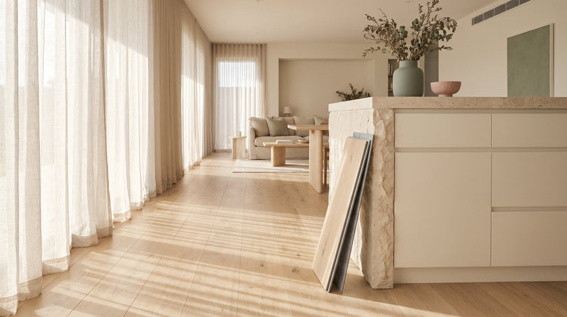 Wide pale oak SPC hybrid floorboards in an open-plan Australian home, with a loose plank showing its rigid stone core
