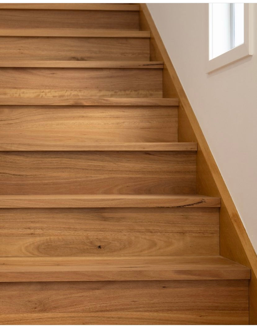 Wooden staircase with a light-colored wall and window in the background