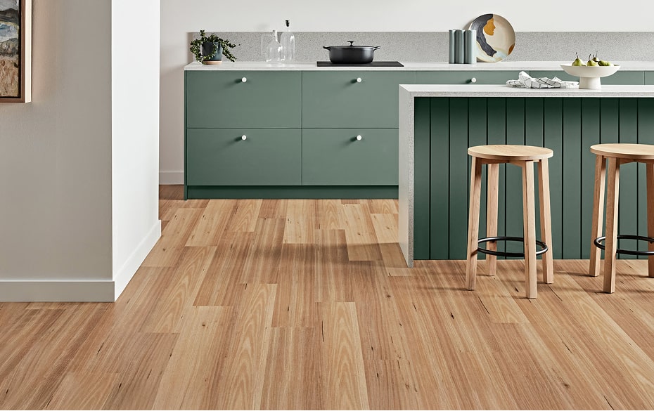 Modern kitchen with green cabinets, wooden floor, and stools.