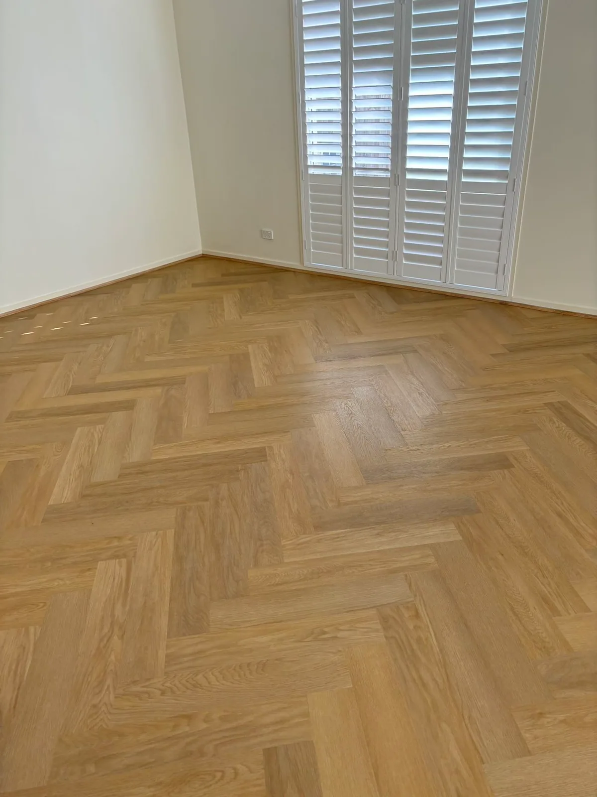 French Oak 9.5mm herringbone hybrid flooring near a room corner and window