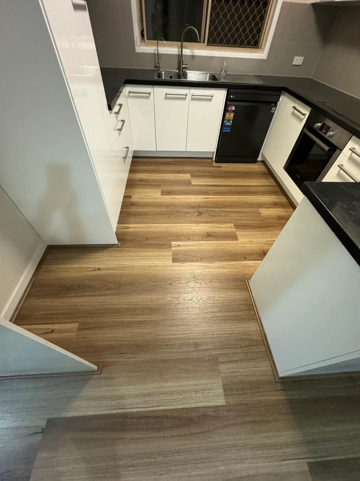 Natural Spotted Gum 9.5mm hybrid flooring beside kitchen cupboards