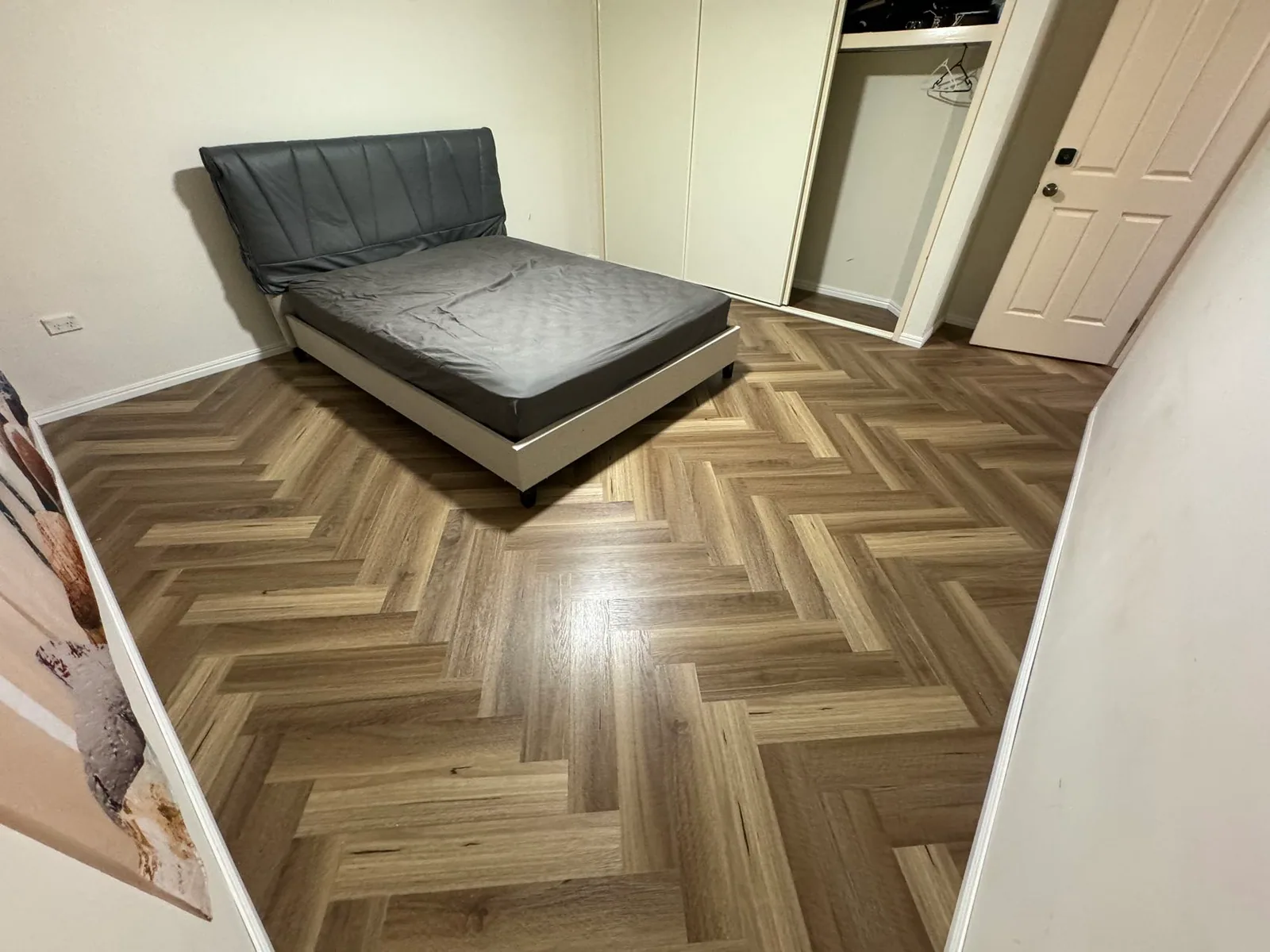 Natural Spotted Gum 9.5mm herringbone hybrid flooring in a bedroom beside a bed