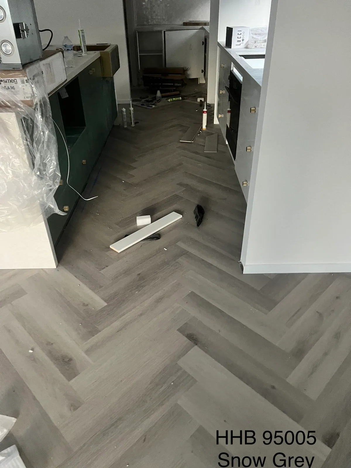 Snow Grey 9.5mm herringbone hybrid flooring during installation beside kitchen cabinets